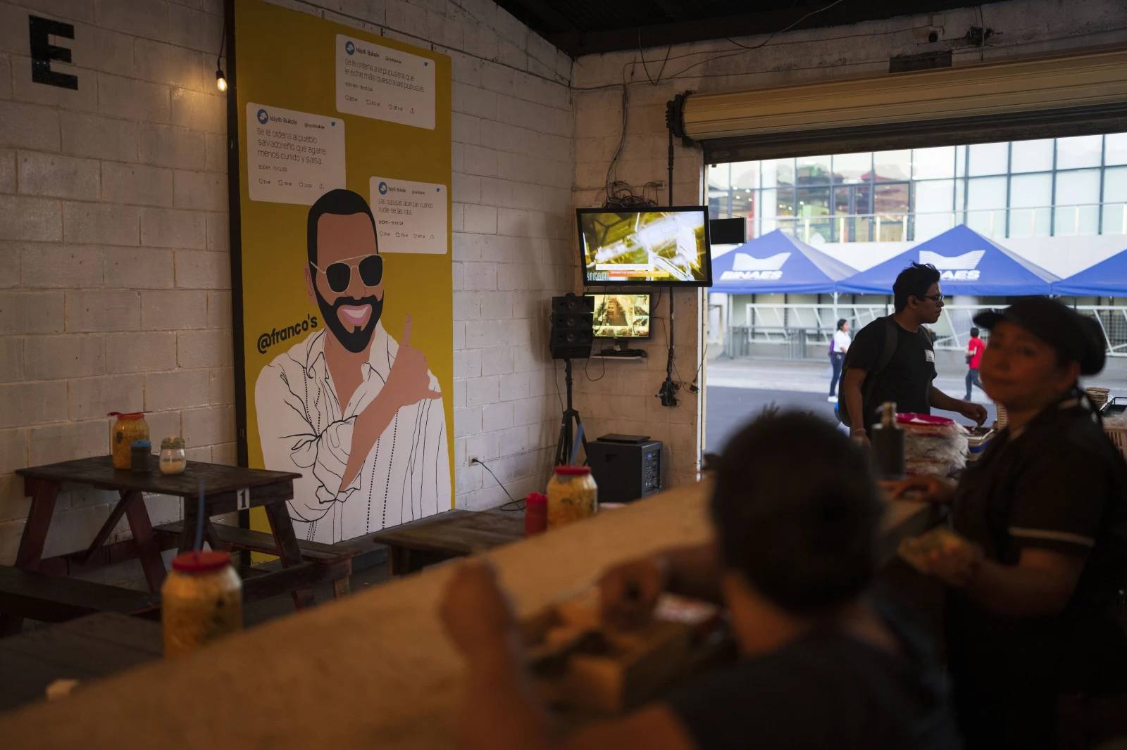Patrons sit at a food store decorated with a mural of El Salvador President Nayib Bukele, who is running for re-election, in downtown San Salvador, El Salvador, Monday, Jan. 29, 2024. (Credit: Moises Castillo/AP.)